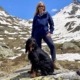 Hiking with cute Animals 1 a woman standing next to a dog in front of a snowy mountain